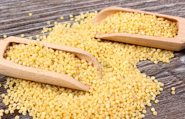 Heap of millet groats with spoon on wooden background