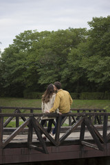 Fototapeta premium Young couple in 20s, leaning on wooden bridge. In nature, park.
