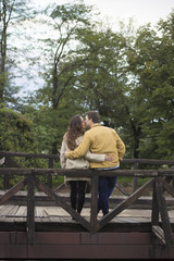 Fototapeta premium Young couple in 20s, leaning on wooden bridge. In nature, park.