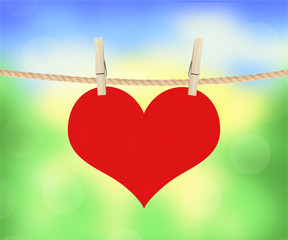 red heart hang on clothespins over blurred nature background