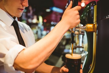 Bartender holding beer glass below dispenser tap