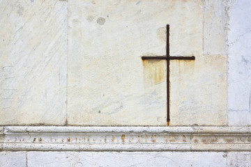 Iron cross snuggled in white stone on a italian facade church