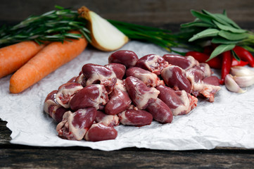 Raw Duck hearts on crumpled paper, decorated with vegetables. on old wooden table