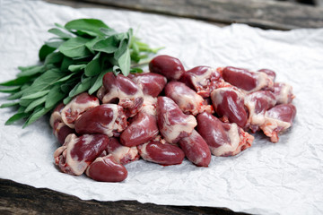 Raw Duck hearts on crumpled paper, decorated with vegetables. on old wooden table