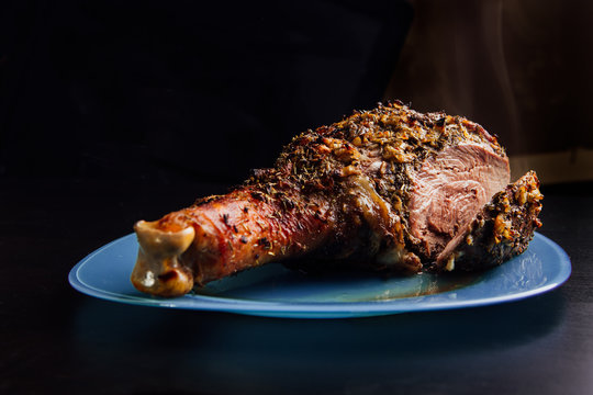 great fresh baked turkey leg sprinkled with spices lying on a blue plate to black wooden background