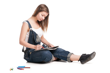 Fototapeta na wymiar Young woman happily sitting on the floor drawing in her note pad