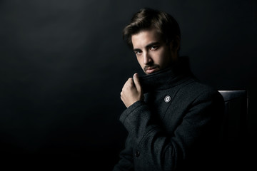 Young handsome man in coat on black background