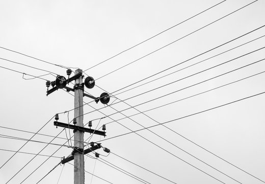 Power lines in black and white - Power transmission lines form a crisscross pattern around a transmission pole on a cloudy day. Black and white image.