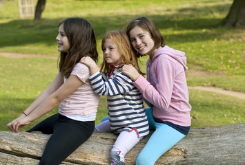 Pretending. Three young girls are pretend playing on a fallen tree. They are obviously friends...