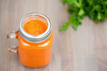 Carrot smoothie in a mason jar with carrots on wooden background