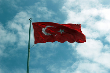 The flag of Turkey waving in the wind over blue sky.