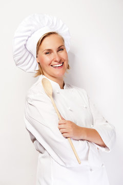 Woman chef in cook outfit holding wooden spoon and smiling at ca