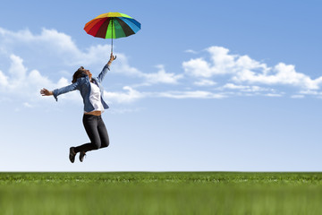 Happy young girl is flying with colorful umbrella on nature