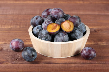 Fresh juicy plums in wooden round bowl