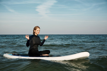 Stand up paddle board yoga performed by beautiful girl on the bright sunset background, yoga...