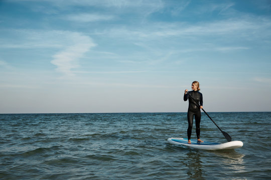 Young blonde female paddles a paddleboard at the sea.