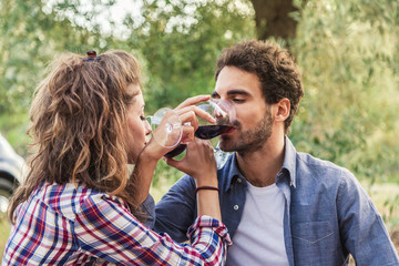 A couple of young lovers, drinking red wine from glass goblets at a picnic in a field in Tuscany,...