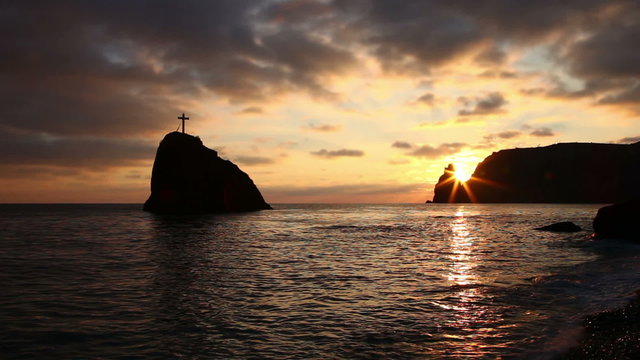 Cross on a rock in the sea, on the coast in the evening