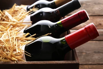 Fototapeten Box with straw and wine bottles on wooden background © Africa Studio