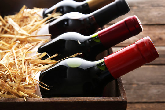 Fototapeta Box with straw and wine bottles on wooden background
