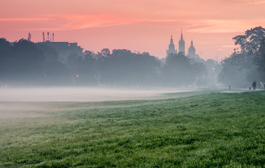 Blonia meadow in Krakow, Poland, with St Mary's church and Town Hall towers in the background, foggy morning.