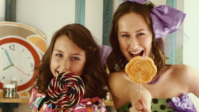 Two girls lick candies and show them in the camera