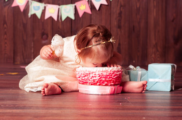 Baby girl 1 year old celebrating first birthday in room. Eating cake. Birthday decoration....