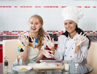 Woman in chef uniform explaining to her younger friend how to make dough