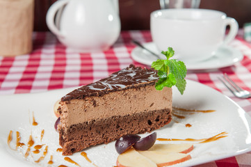 Close up Chocolate Cheesecake with fruits and  Green Mint on the white plate on the served  restaurant table 