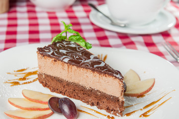 Close up Chocolate Cheesecake with fruits and  Green Mint on the white plate on the served  restaurant table 