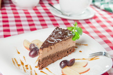 Close up Chocolate Cheesecake with fruits and  Green Mint on the white plate on the served  restaurant table 