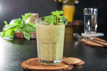 Glass of healthy green vegetable smoothie on the wooden board on dark background