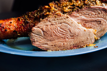 great fresh baked turkey leg and sliced piece sprinkled with spices lying on a blue plate to black wooden background