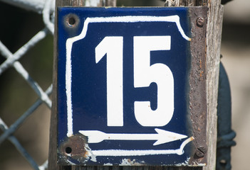 Weathered grunge square metal enameled plate of number of street address with number 15 closeup