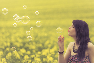Beautiful woman blowing many soap bubbles in summer nature. The girl has fun in a yellow meadow and is enjoying her youth