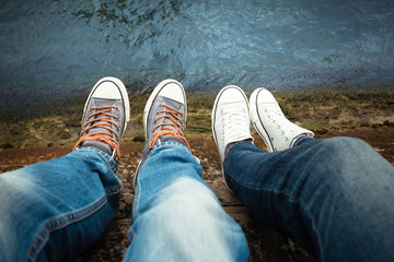Close up of male and female's feet relaxing by the river - obrazy, fototapety, plakaty