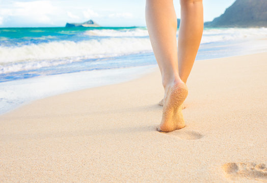 Closeup of woman walking on sand beach leaving footprints in the sand. Closeup