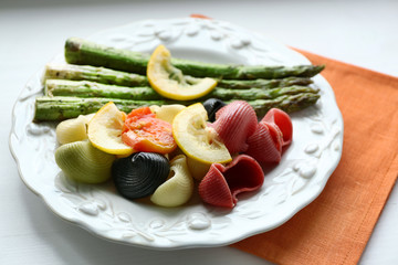Roasted asparagus and tasty colorful pasta with vegetables on plate on wooden table background