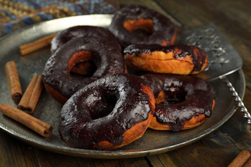 Delicious doughnuts with chocolate icing and cinnamon on metal tray close up