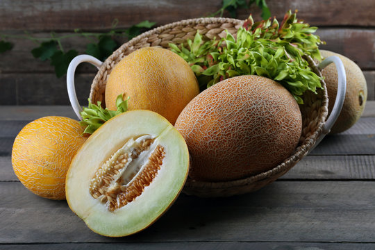Ripe melons with green leaves in basket on table close up