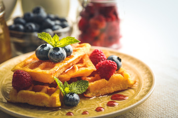 Sweet homemade waffles with forest berries and sauce on table background