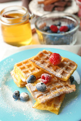 Sweet homemade waffles with forest berries on plate, on light background