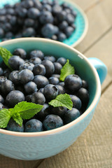 Cup and plate with fresh blueberries on wooden table close up