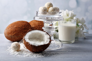 Candies in coconut flakes and fresh coconut on color wooden table, on light background