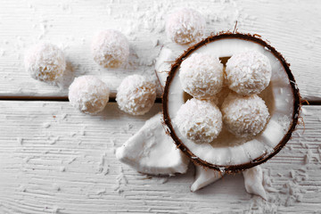 Candies in coconut flakes and fresh coconut on  light wooden background © Africa Studio