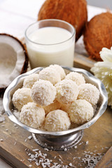 Homemade sweets in coconut flakes and fresh coconut on tray, close-up