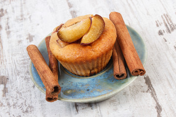 Fresh baked muffins with plums and cinnamon sticks on old wooden background, delicious dessert