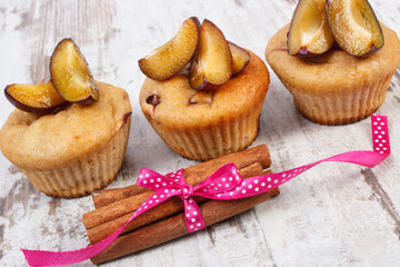 Fresh baked muffins with plums and cinnamon sticks on old wooden background, delicious dessert