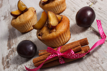 Fresh baked muffins with plums and cinnamon sticks on old wooden background, delicious dessert