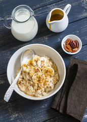 oatmeal with banana, caramel sauce and pecan nuts in a white bowl on a dark wooden surface, a delicious and healthy Breakfast